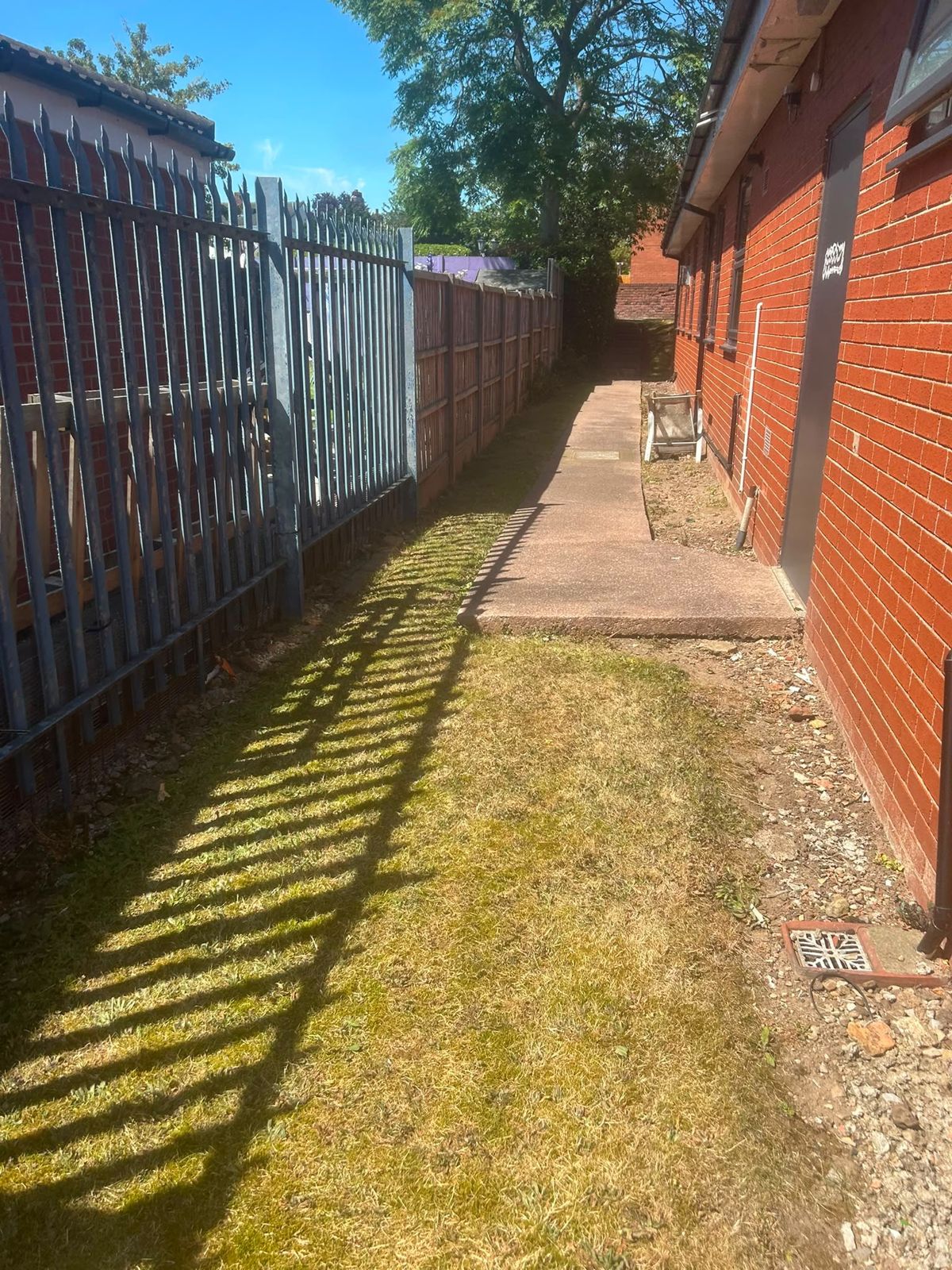 Cut grass strip between fencing and a brick building